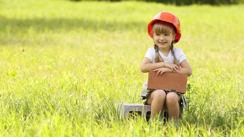 Construction is cool. The little girl in the construction helmet sits on cinder block. Thumbs up
