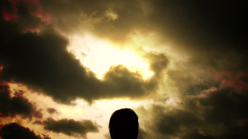 Person silhouetted raises walks up to camera, raises his hooded sweatshirt and dissolves into thin air in a dark, eerie fiery setting.