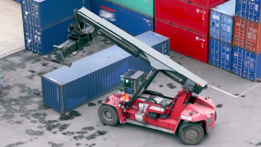 Driver takes seat in crane cabin and drives backward among containers at seaport