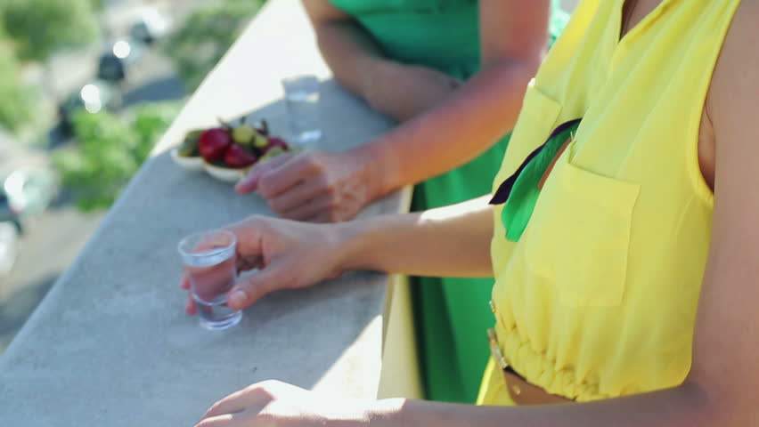 Female friends talking and drinking vodka shots on terrace
