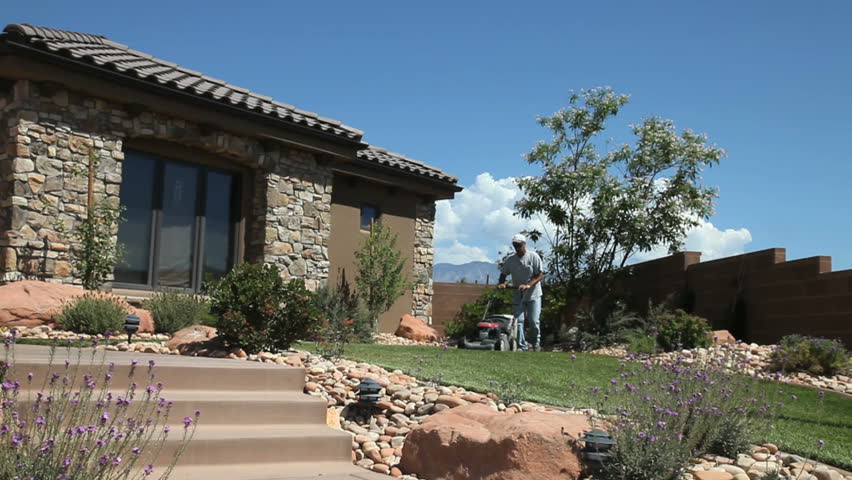 Man cutting lawn with power mower in front of home with flagstone siding
