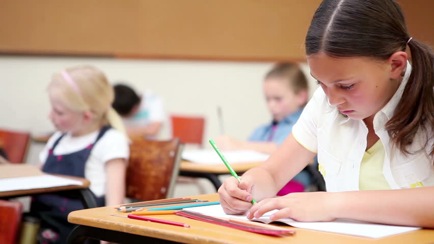 Pupil writing on her notebook in the classroom