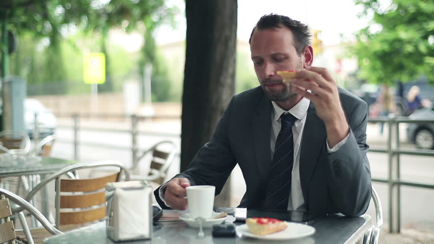 Young businessman eating breakfast in cafe by the street
