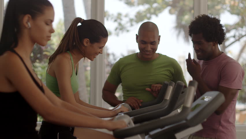 Sport and fun, group of young men and women talking and laughing in gym while working out and exercising on bikes