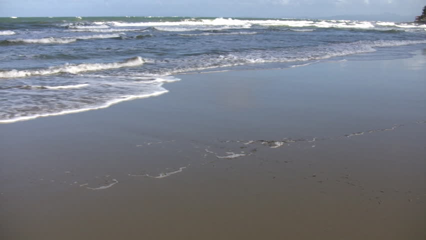 Waves gently wash up onto the beach, then recede as the sunlight illuminates the surf. (High Definition)
