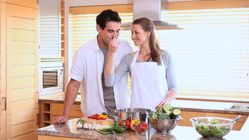 Husband tasting his wife's cooking with a spoon in a kitchen