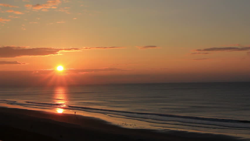 Spectacular beach sunrise from high rise seen from several stories up.  A man who is in silhouette is walking alone on the beach below.