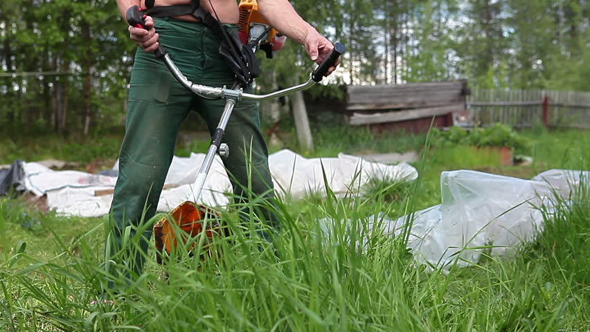 Unrecognizable man starting engine by petrol trimmer and mowing overgrown green grass 