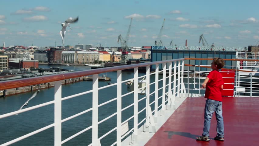 Little boy throws pieces of bread to feed gulls in port at sunny day