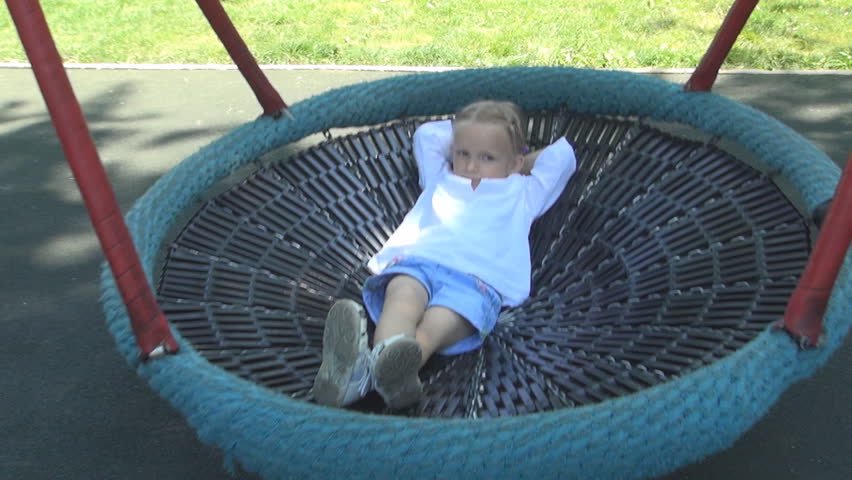 A Happy Little Girl is Playing, Swinging on a Swing Set in a Playground