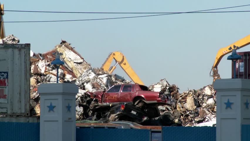 Cranes lift and move scrap metal around abandoned and destroyed cars in a junkyard or scrap metal yard.