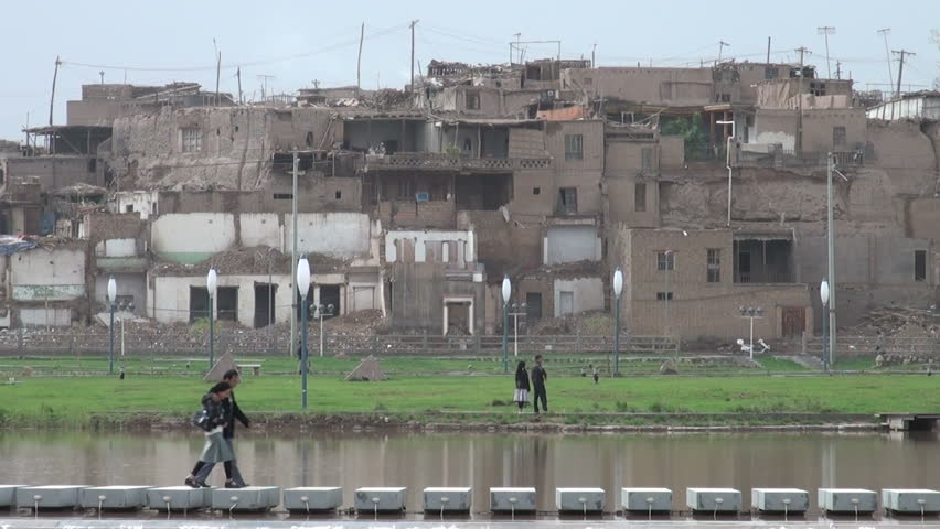KASHGAR - SEPTEMBER 20 2010: A couple walks over new foundations with the soon to be demolished old town of Kashgar in the background