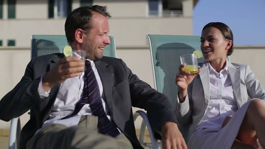 Happy business couple with drinks relaxing on sunbeds
