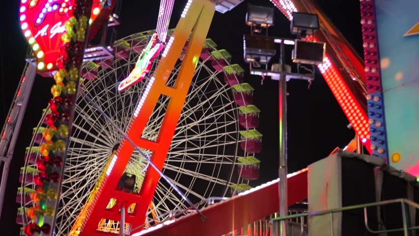 Panning view of a large swinging ride in an amusement park at night, with changing flashing lights.