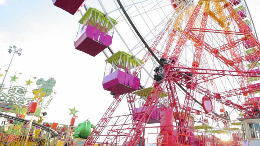 Colorful ferris wheel turning with the sun filtering through it and shining at an amusement park in the daytime.