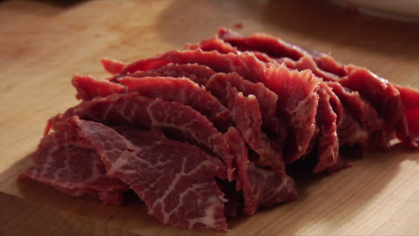 Close-up, slow pan over slices a Flat Iron steak and chef placing the slices on a plate.