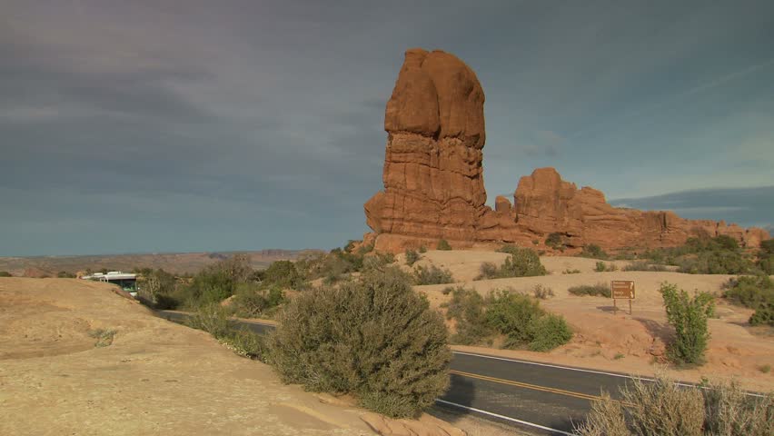 RV driving past Balanced Rock formation at Arches 