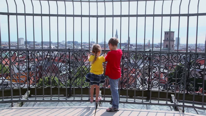 Two kids boy an little girl hang on lattice with cityscape beyond