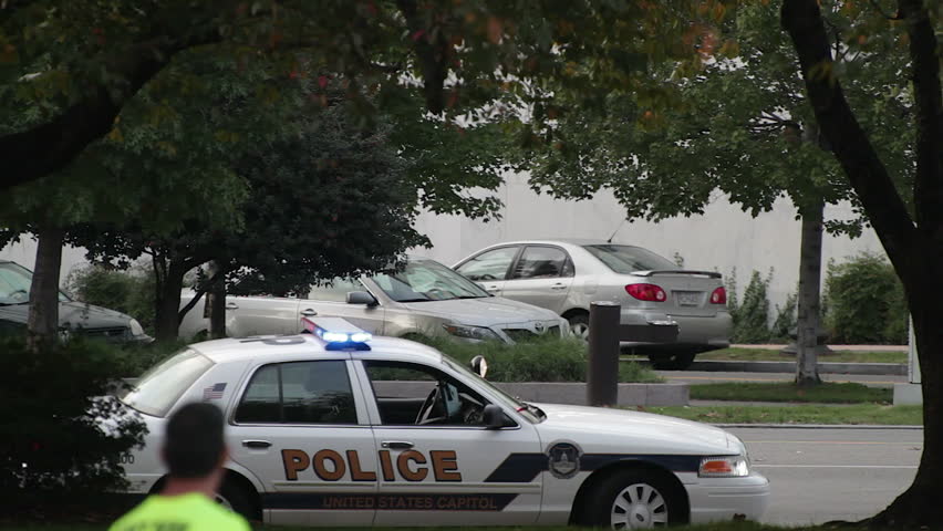 Washington DC, USA - October 23: A police car parked at a downtown road, its siren lights flash on October 23, 2011. Another police car and traffic drives past. A curious onlooker in the foreground watches the scene.