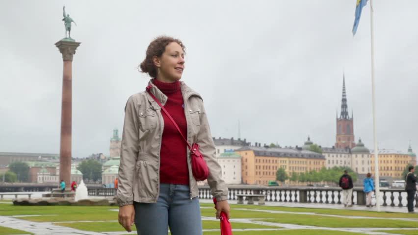 Woman stand on square with fountain and monument at river quay in Stockholm