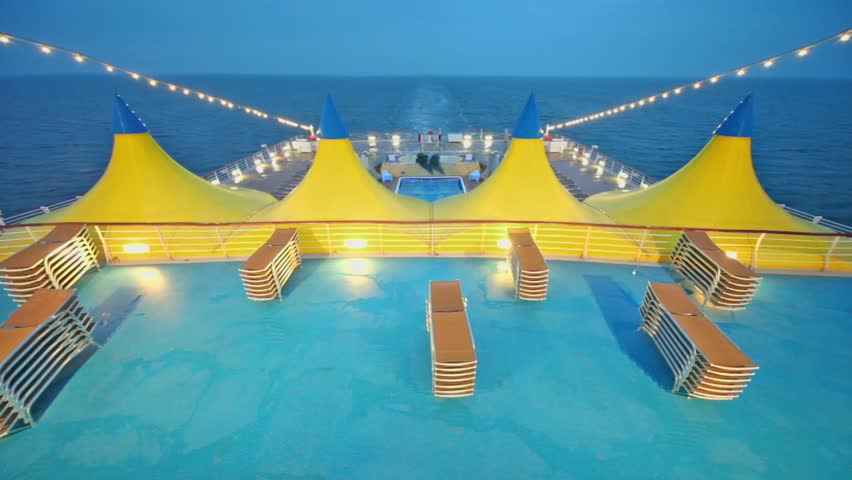 Deckchairs near pool and tents on empty deck of ship which float in sea at evening during cruise 
