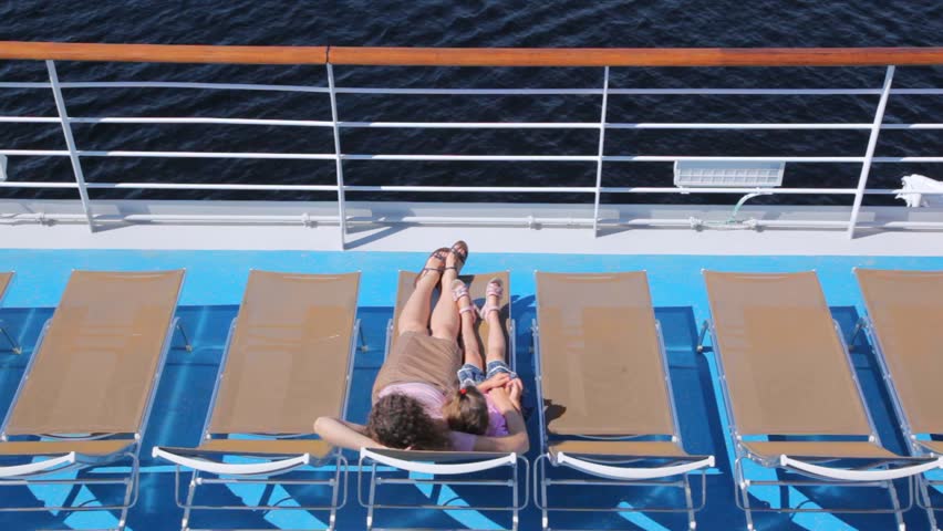 Mother with daughter lie in chaise lounge on liner deck
