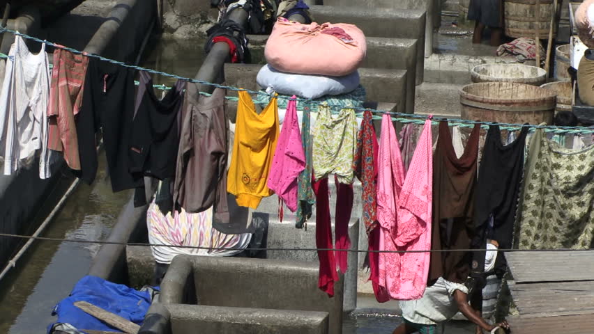 Washing hanging in a open air laundry at a slum in India.  Man in the background washing clothes in a basin.
