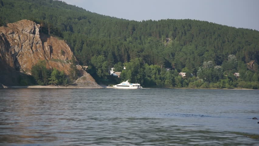 White pleasure boat is at the rocky shore of the Siberian river Yenisei. Natural landscape, static shot.