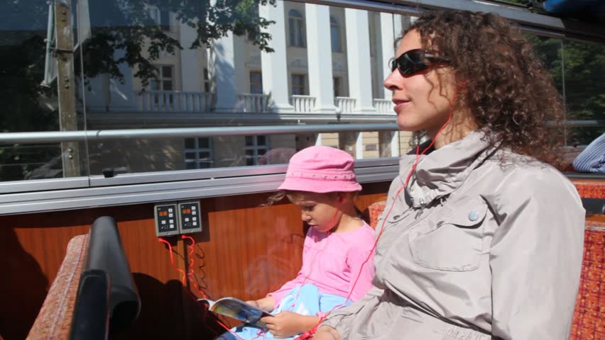 mother in tourist bus tells to daughter something, at which in hands guidebook around city to Tallinn