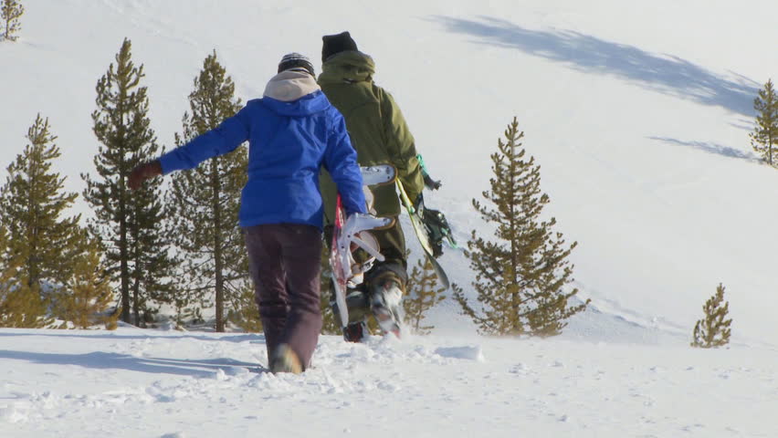 Male and female snowboarders hike through back-country powder