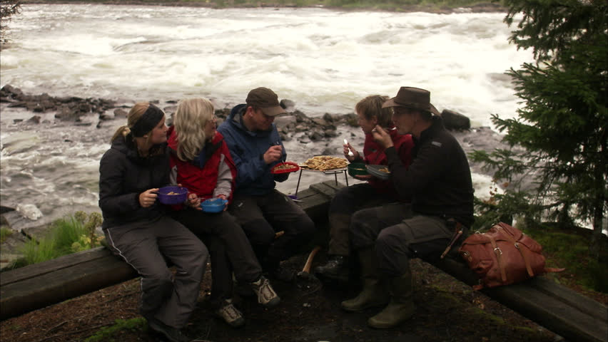 People eating sitting around a camp fire