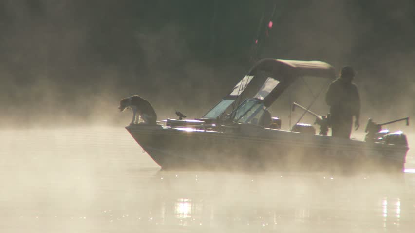 NEW ENGLAND - CIRCA APRIL 2009: Mist rising from early morning pond with dog sitting on bow of fishing boat