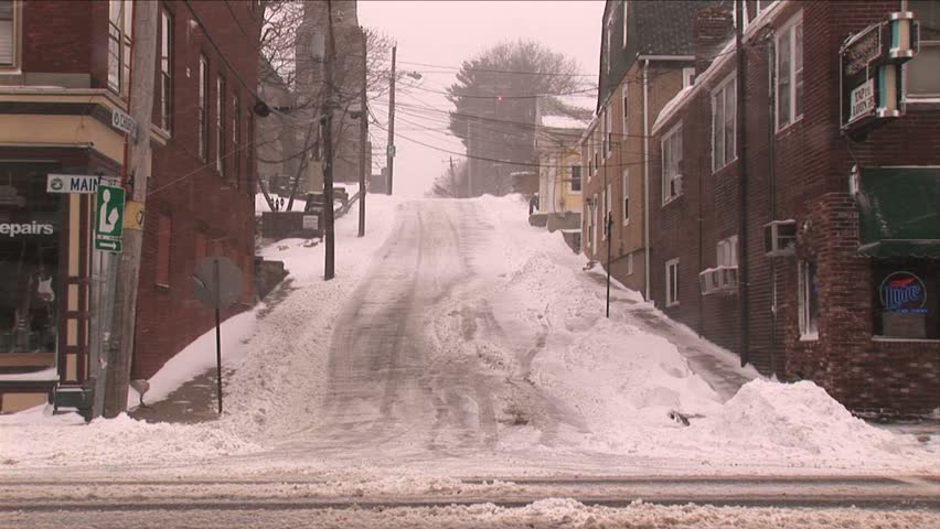 NEW ENGLAND - CIRCA JANUARY 2006: Snowplow passing by snowy hillside downtown street