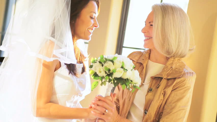 Proud mother hugging daughter in wedding dress at home before ceremony soft lighting