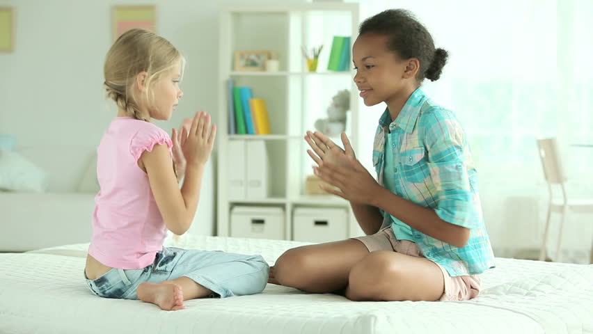 Cheerful girls sitting on the bed and clapping hands playing the game of pat-a-cake