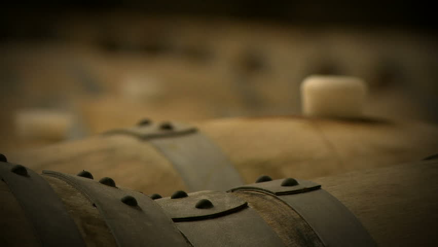 Rack focus along the tops of wine barrels, aging in the cellar of a winery.