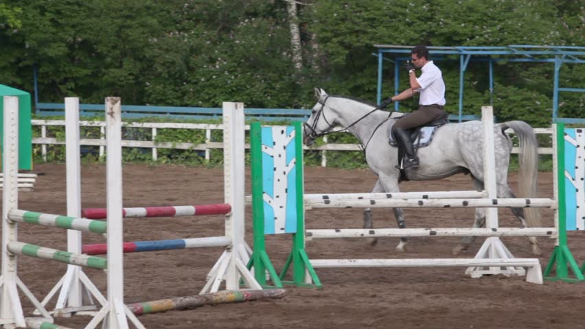Jockey rides on horseback equestrian field among bars and other equipment