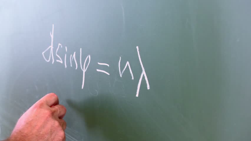 Hand writes formulas of diffraction lattice on green board, closeup view in classroom