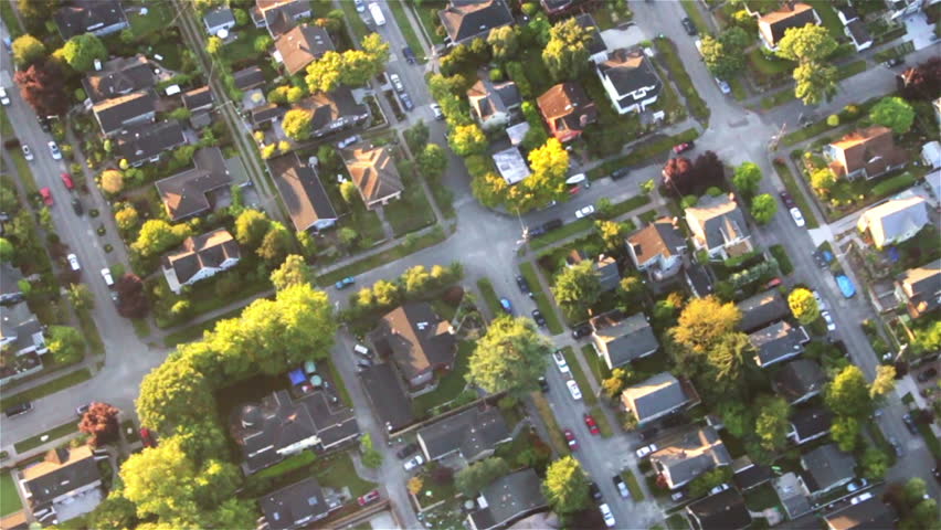Overhead right pan across houses, yards and cars along suburban street