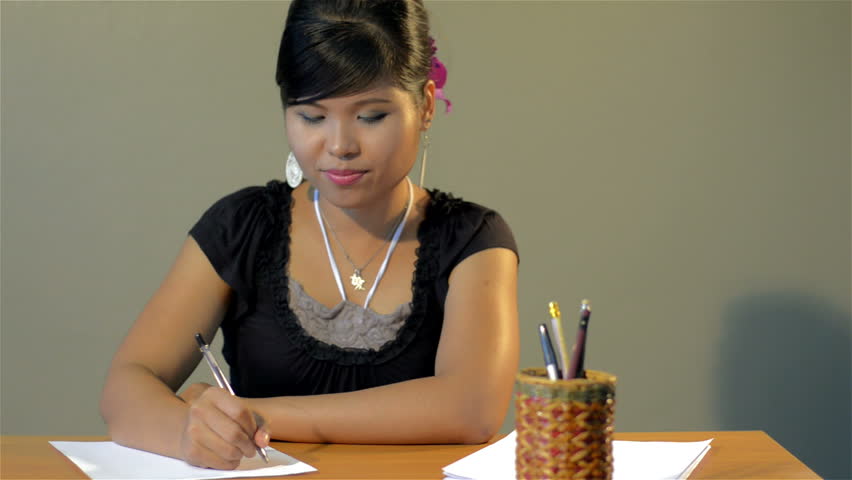 A young Asian woman frustrated writing, so she screws up the paper and tries again. Vintage style - dolly tracking shot.