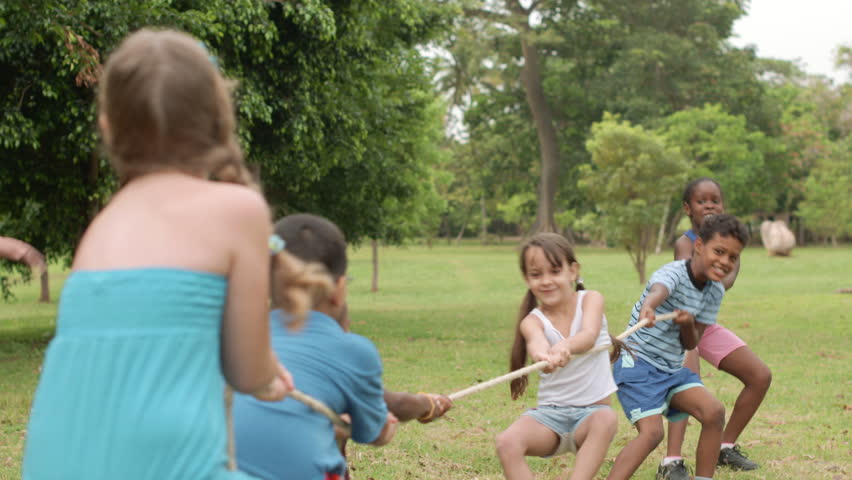 Children and recreation, group of happy multiethnic school kids playing tug-of-war in city park with teacher. Summer camp fun