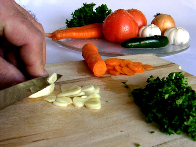Sliding garlic for tomato sauce.  Represent preparation of ingredients for old recipe tomato sauce popular in East-South part of Europe. Carrots and Parsley are already chopped.