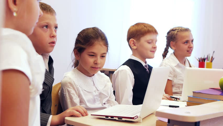 Happy young pupils sitting at the table and chatting during studying on laptops 