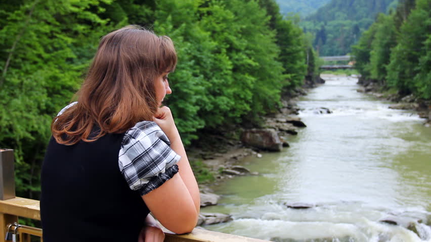 pretty woman stands near railing bridge and looks on waterfall in Carpathian Mountains, closeup