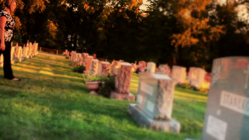 A woman visits a grave in a cemetery.