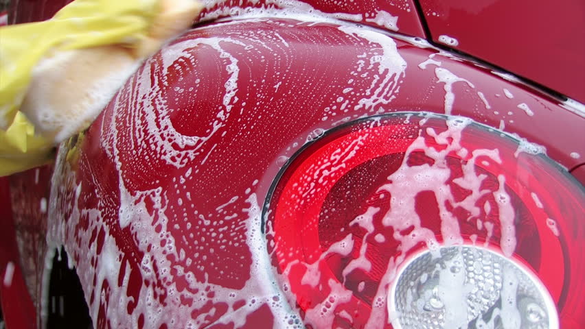 washing car rear lamp by hand with a yellow sponge waring yellow protective gloves
