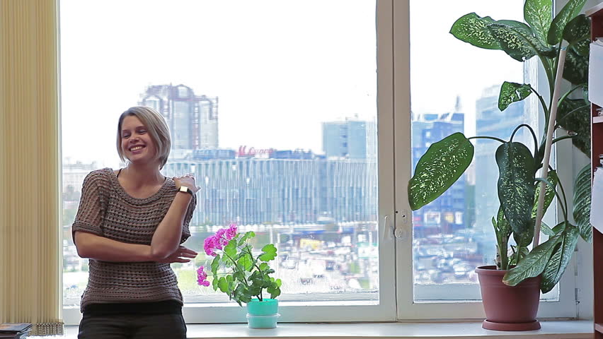 Caucasian female sitting along on windowsill in domestic room talking and looking at camera