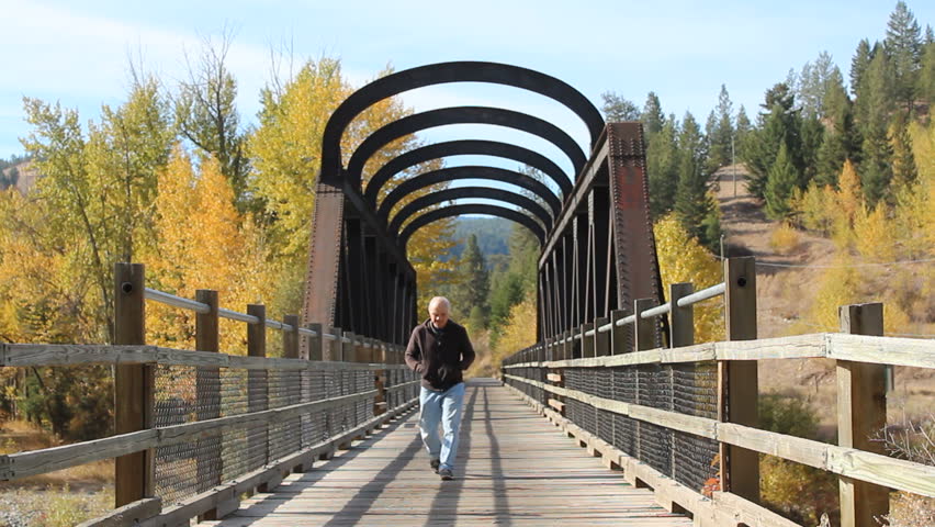 A tourist walks across an old train bridge that was part of the Kettle Valley Railroad, a heritage site in British Columbia, Canada/Tourist and Rail Bridge/The Kettle Valley Railroad