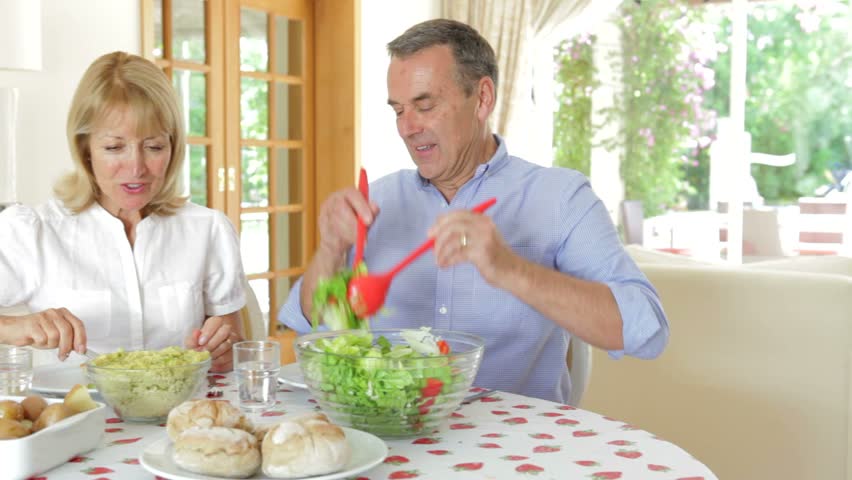Senior couple seated around dining table serving one another.