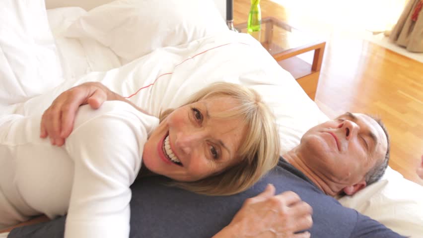Senior woman lying on husbands chest and looking into camera.
